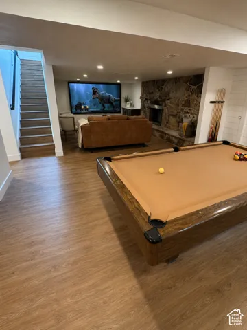 Entertainment area featuring wood-finish flooring, a stone-clad fireplace, a large projection screen, recessed lighting, and white shiplap accent walls