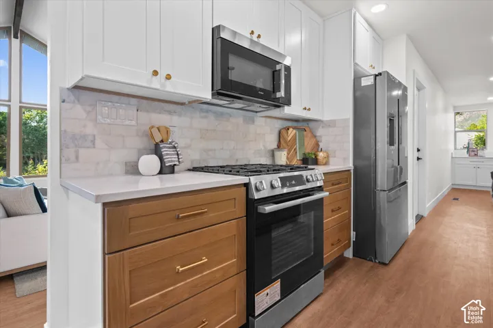 Kitchen featuring white upper cabinetry, wood-finish lower cabinetry, a stone tile backsplash, and stainless steel appliances