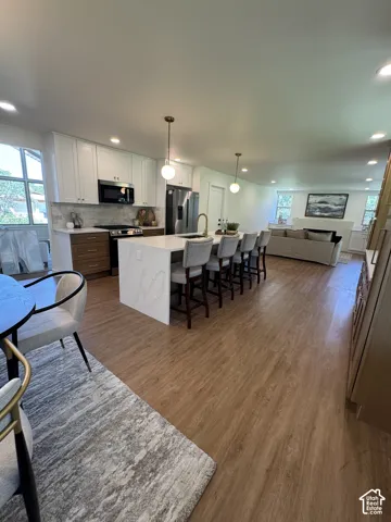 Open-concept living space with wood-finish flooring, recessed lighting, and a kitchen island featuring a waterfall countertop