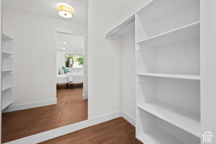 Walk-in closet featuring built-in shelving, hanging rod, and wood-finish flooring