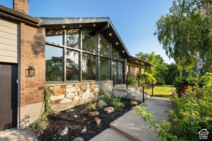 Contemporary exterior with a prominent brick chimney, large floor-to-ceiling windows, and a natural stone façade