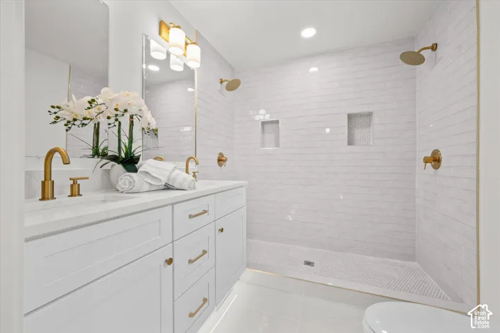 Bright bathroom featuring a double vanity with white cabinetry, gold-finish hardware, and a quartz countertop
