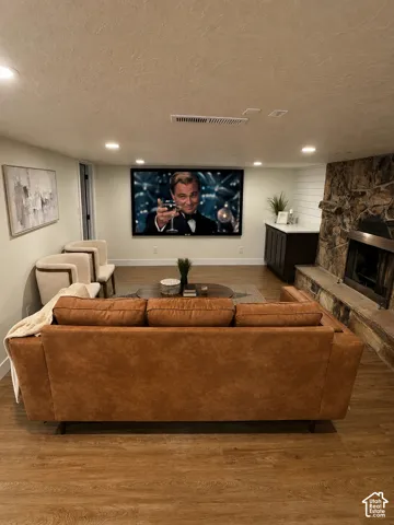 Entertainment space featuring a large wall-mounted screen, wood-finish flooring, recessed lighting, and a stone-clad fireplace