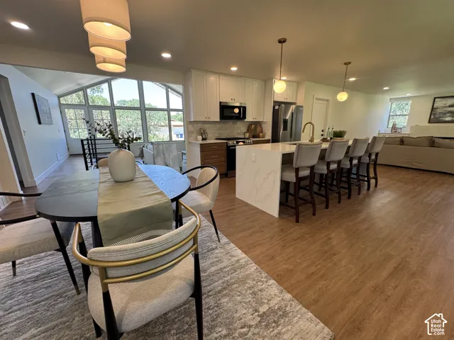 Expansive wood-finish flooring throughout, complemented by a kitchen island with seating for four, stainless steel appliances, and white cabinetry