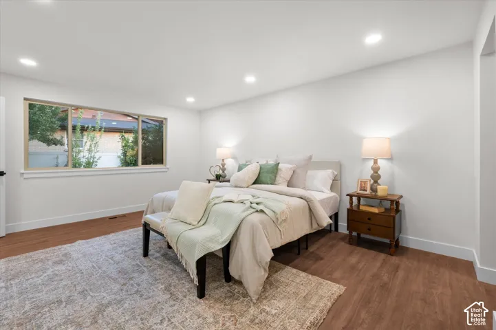 Spacious room featuring wood-finish flooring, a large window, recessed lighting, and white baseboards