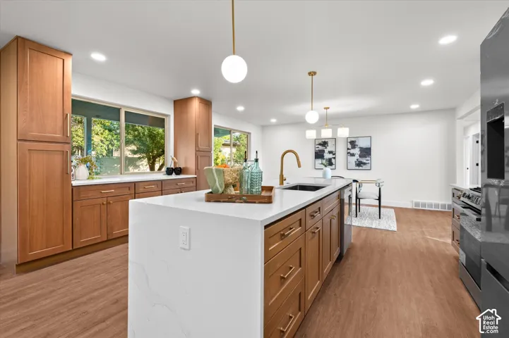 Modern kitchen featuring a large center island with a white countertop and integrated sink, gold-finish fixtures, wood-finish flooring, and recessed ceiling lighting