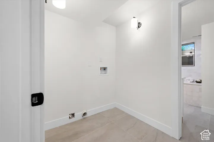 Dedicated utility space featuring tile flooring, white walls, and a modern wall sconce