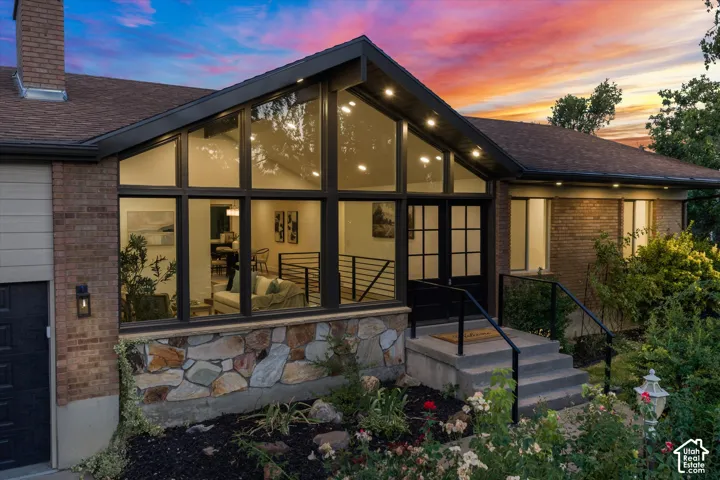 Contemporary exterior featuring a striking A-frame window wall, brick and stone facade, dark-frame windows, and a black double-door entry