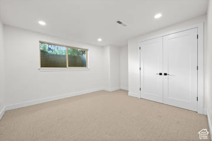 Carpeted room featuring a window with a window well, recessed lighting, and a pair of panel doors with matte black hardware