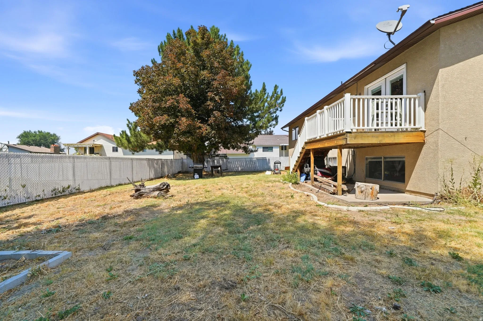 Rear exterior featuring a wood deck with white railings, a lower-level concrete patio, and a large mature tree