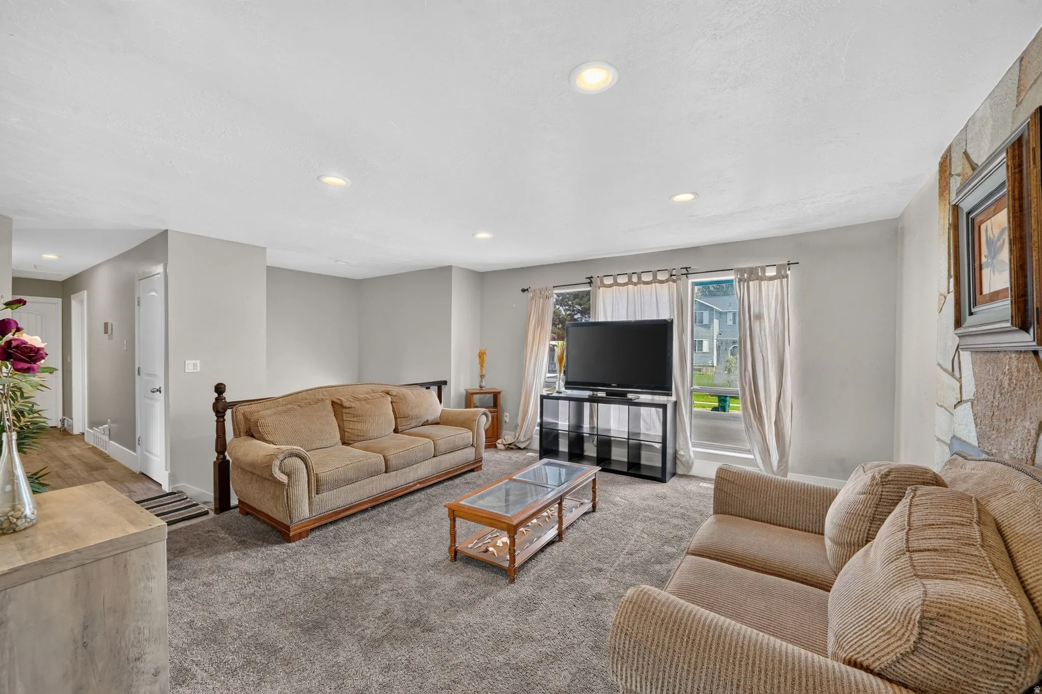 Recessed ceiling lighting, gray carpeting, stone-clad accent wall, large windows, and light gray wall paint