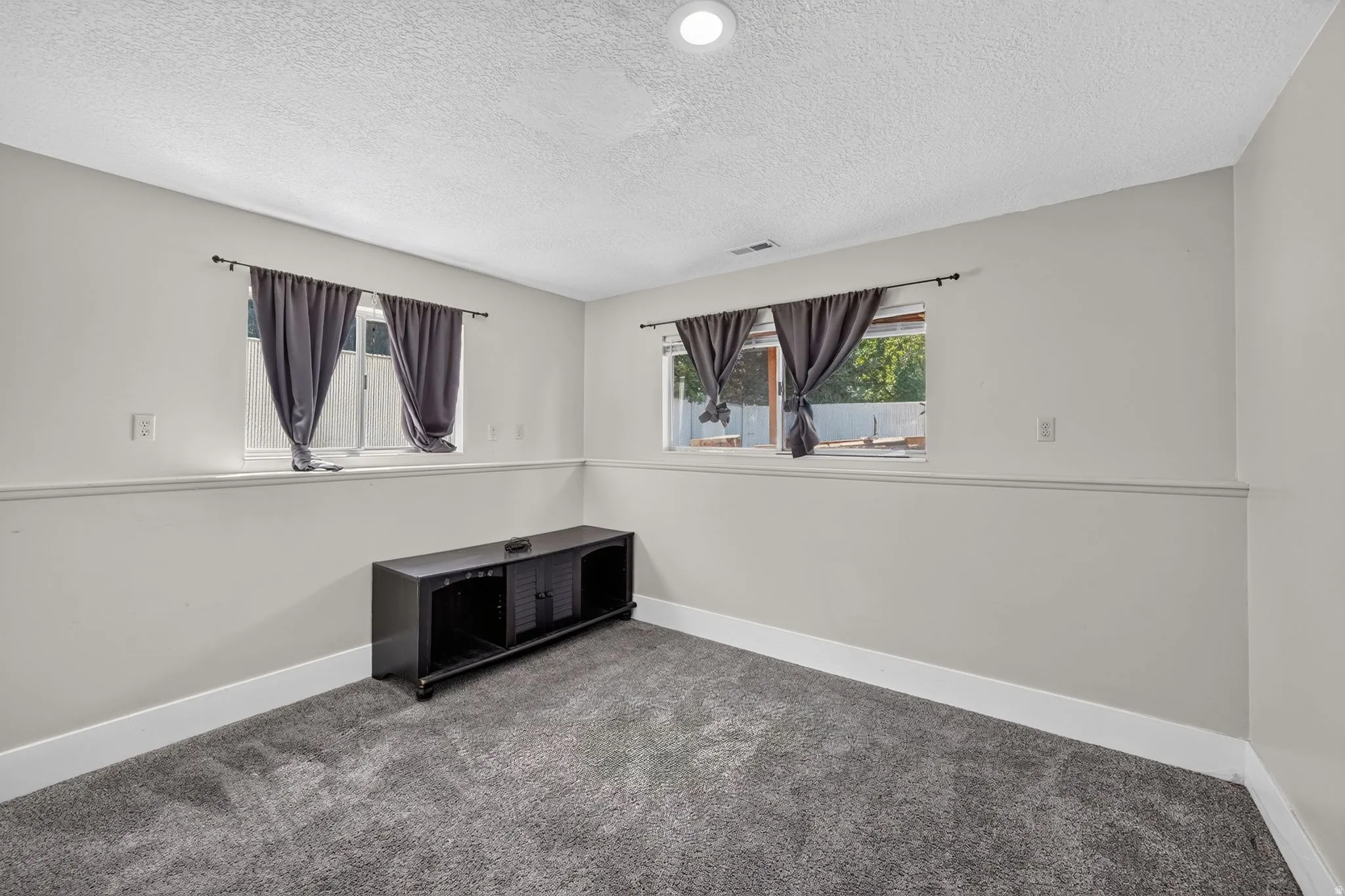 Recessed lighting, two windows, textured ceiling, light gray walls, and gray carpet