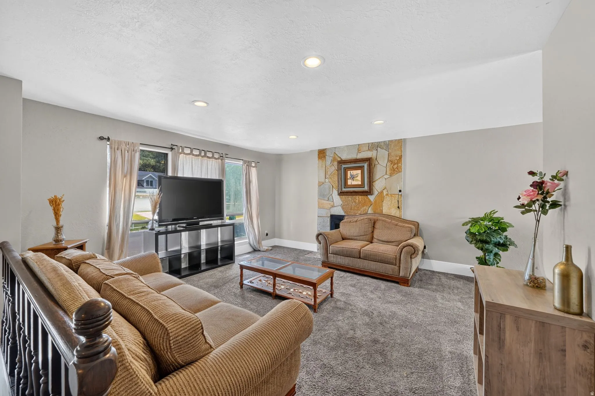 Recessed lighting, stone-clad fireplace wall, large windows with natural light, and carpeted flooring