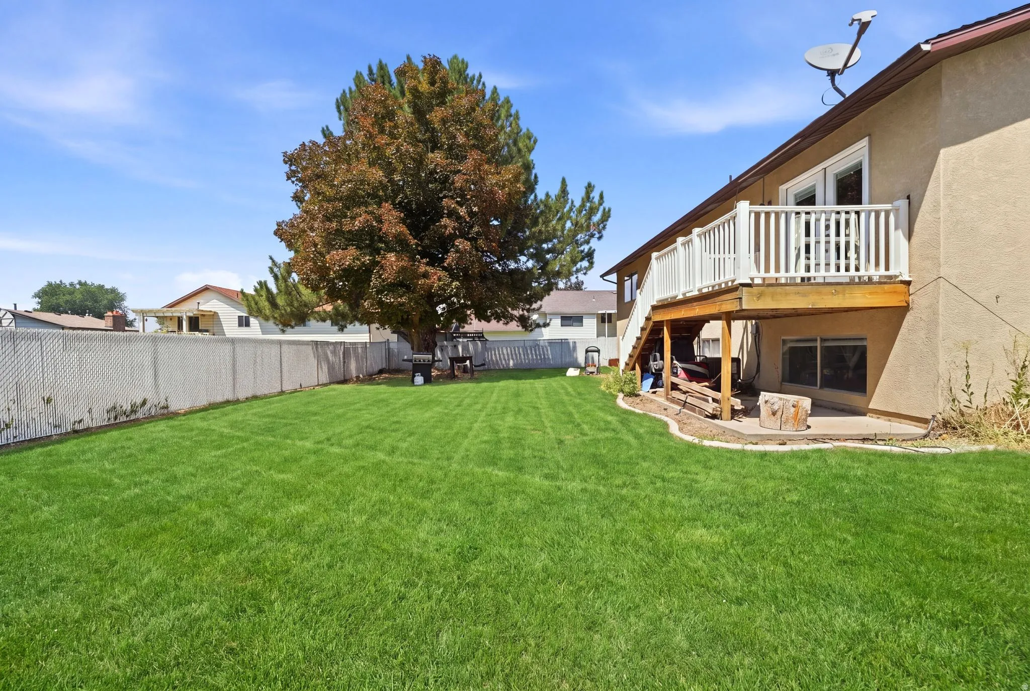 Expansive lawn space, private deck with white railing, mature trees, and a ground-level patio