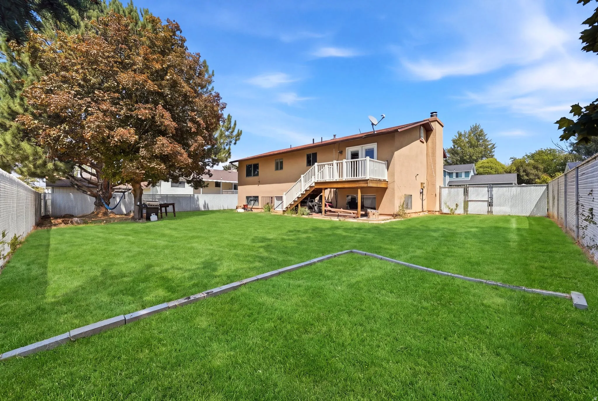 Expansive backyard with a large lawn, mature trees, and a two-story exterior featuring a balcony with railings