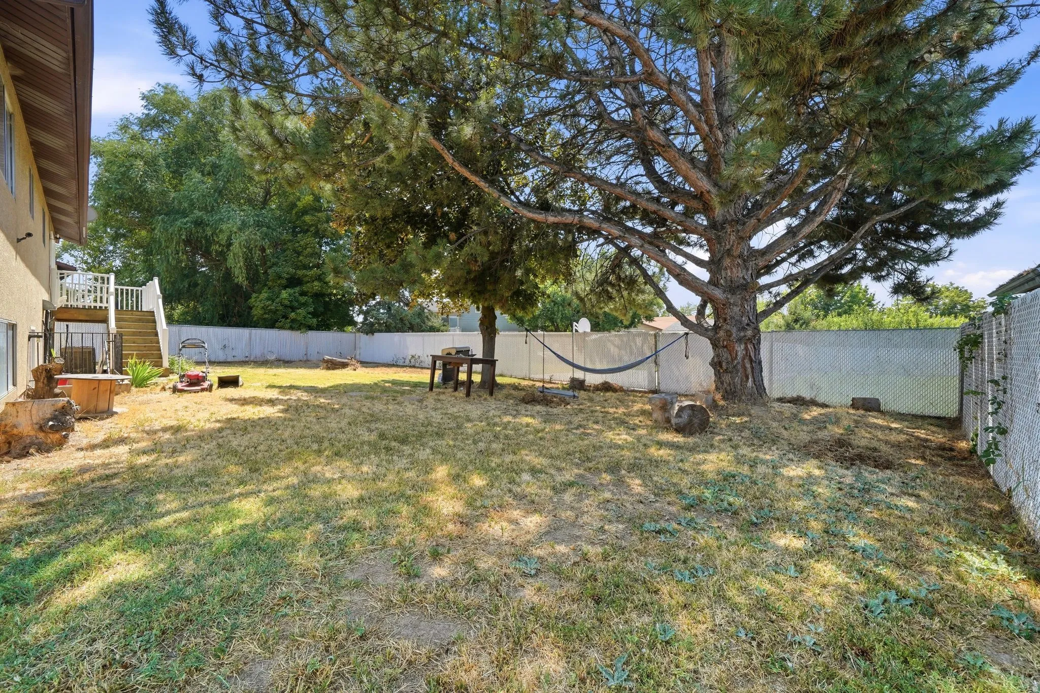 Expansive backyard oasis featuring a mature shade tree, level lawn, white vinyl fencing, and a detached storage structure