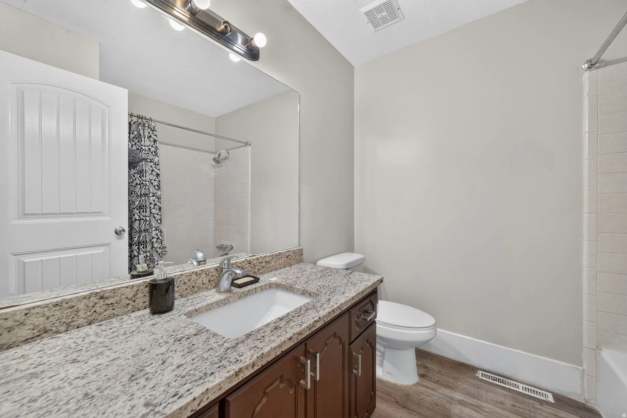 Granite-finish vanity with an undermount sink, wood-finish cabinetry, and a full-width mirror