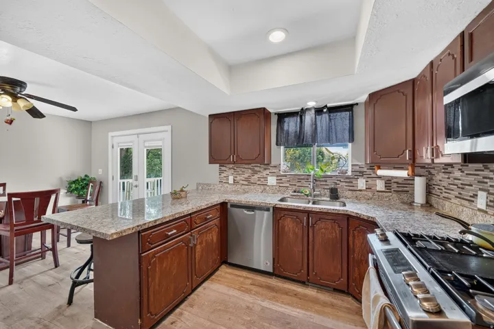Kitchen featuring wood-finish flooring, granite countertops, wood cabinetry, stainless steel appliances, and a mosaic tile backsplash