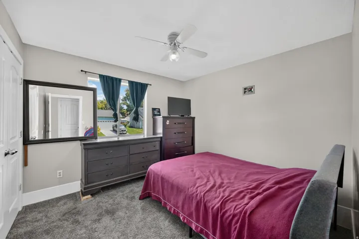 Spacious bedroom featuring carpet flooring, ceiling fan with integrated lighting, and dark wood dresser with mirror