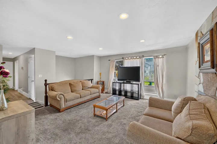 Recessed ceiling lighting, gray carpeting, stone-clad accent wall, large windows, and light gray wall paint