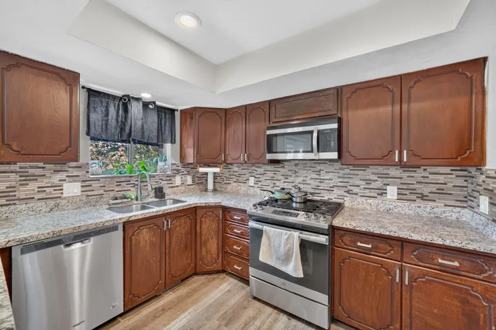 Kitchen featuring wood cabinetry, stainless steel appliances, a double basin sink, light-colored countertops, and a tiled backsplash