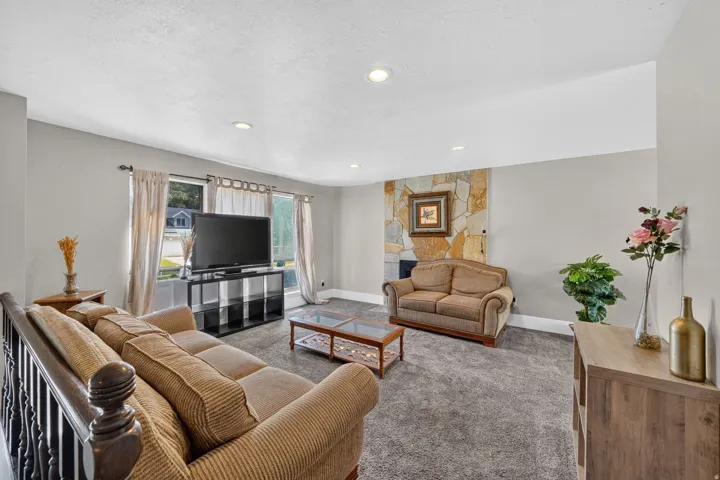 Recessed lighting, stone-clad fireplace wall, large windows with natural light, and carpeted flooring