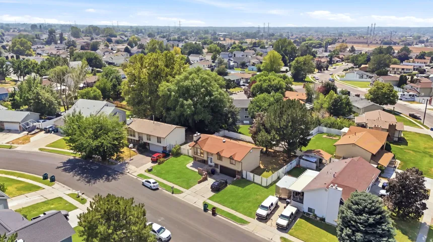 Aerial view showcasing a well-appointed residential property featuring a manicured lawn, mature shade trees, and a brick exterior with an attached garage