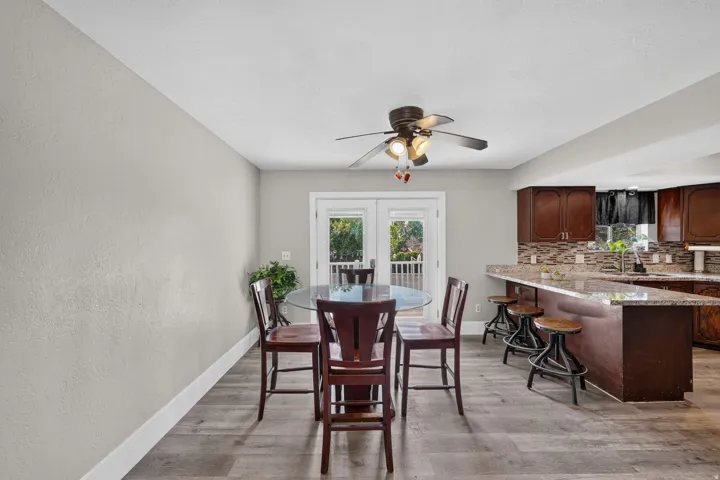 Wood-finish flooring, ceiling fan with integrated lighting, double French doors, kitchen island with bar seating, and wood cabinetry with a tile backsplash
