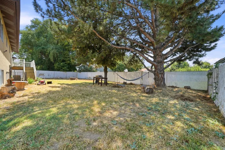 Expansive backyard oasis featuring a mature shade tree, level lawn, white vinyl fencing, and a detached storage structure