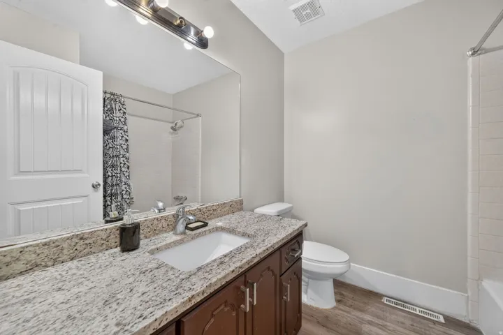 Granite-finish vanity with an undermount sink, wood-finish cabinetry, and a full-width mirror
