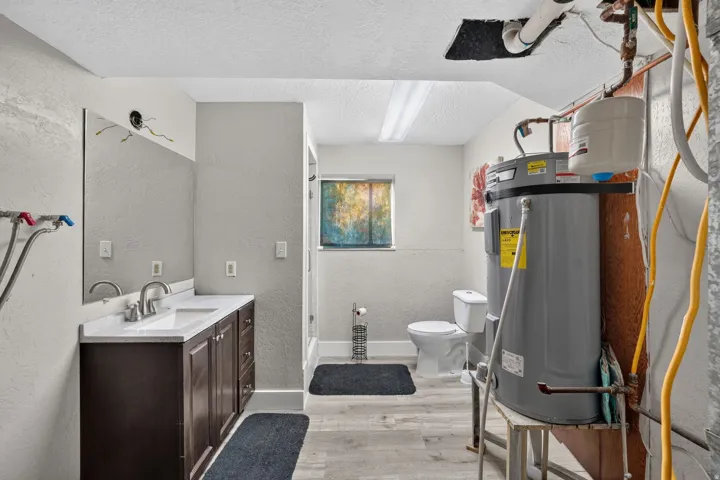 Renovated full bathroom featuring a dark wood vanity with dual sink basin, ceramic tile flooring, white subway tile walls, toilet with black mat, recessed lighting, and utility storage shelving