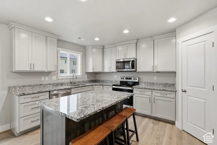 Kitchen featuring light-toned cabinetry, granite countertops, stainless steel appliances, a center island, and wood-finish flooring