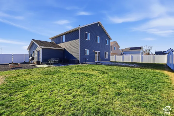 Spacious backyard featuring a manicured lawn, white vinyl fencing, a patio area, and a fire pit