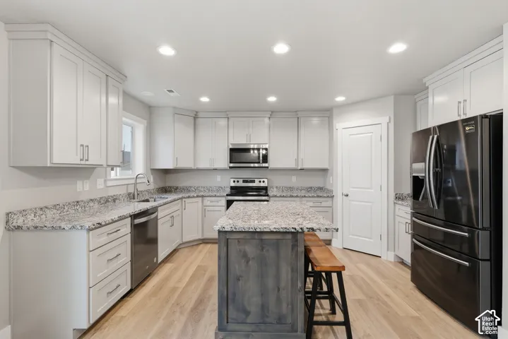 Modern kitchen featuring light wood-finish flooring, white cabinetry with crown molding, and granite countertops