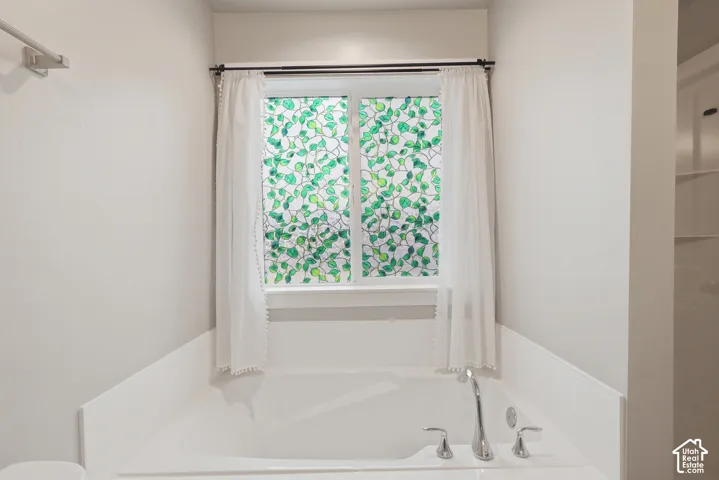 Built-in soaking tub with chrome fixtures and an overhead window featuring a decorative privacy film