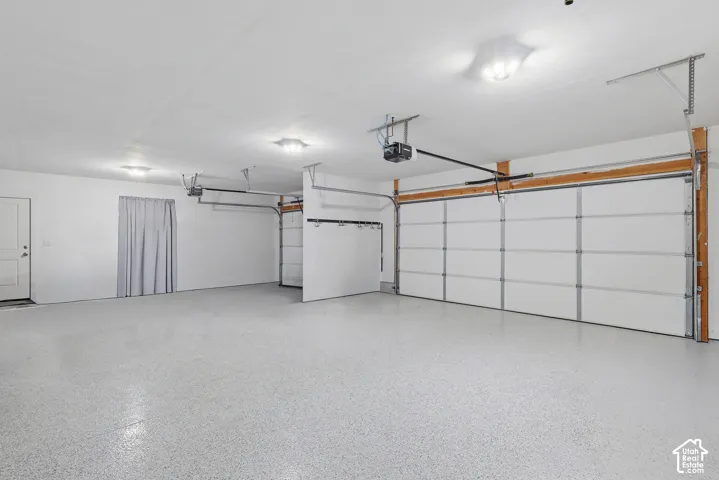 Spacious garage featuring a durable epoxy speckled floor, two overhead garage doors with automatic openers, ceiling-mounted lighting, and an additional access door