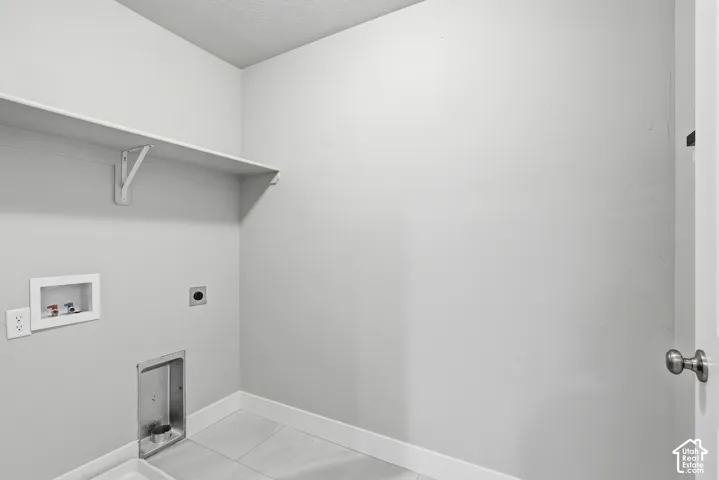 Dedicated laundry area featuring a neutral color palette, integrated wall shelving, utility hookups, and light-toned tile flooring
