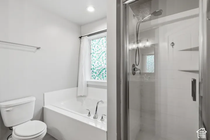 Bathroom featuring a glass-enclosed shower with integrated shelving, a separate soaking tub with chrome fixtures, a single toilet, and a window with privacy glass