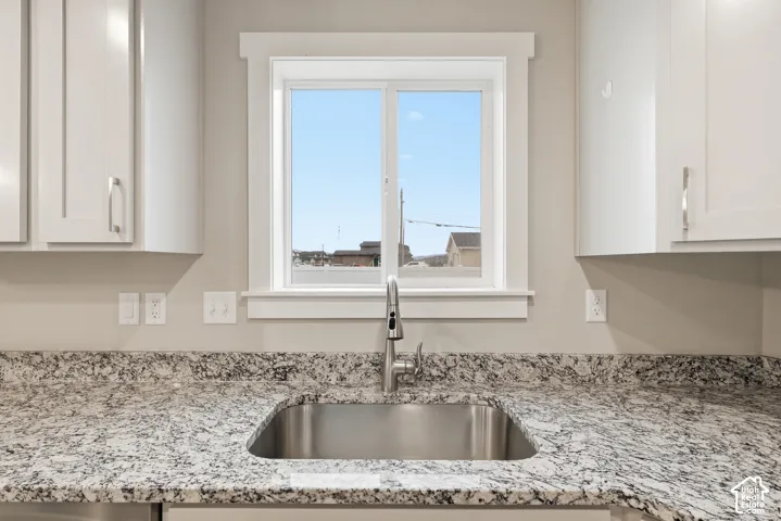 Kitchen sink area featuring a stainless steel undermount sink, gooseneck faucet, light-toned patterned countertops, white shaker-style cabinetry, and a window with white trim