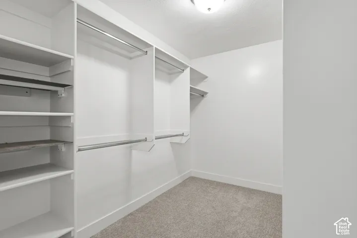 Walk-in closet featuring built-in white shelving, multiple hanging rods, and light gray carpeting