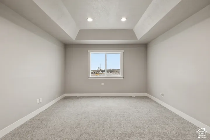 Tray ceiling featuring recessed lighting and a window with white trim, complemented by light gray walls, white baseboards, and gray carpeting