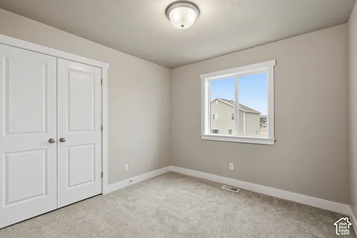Neutral-toned room featuring a double-door closet with panel detailing, a window with white trim, light gray walls, and plush carpeting