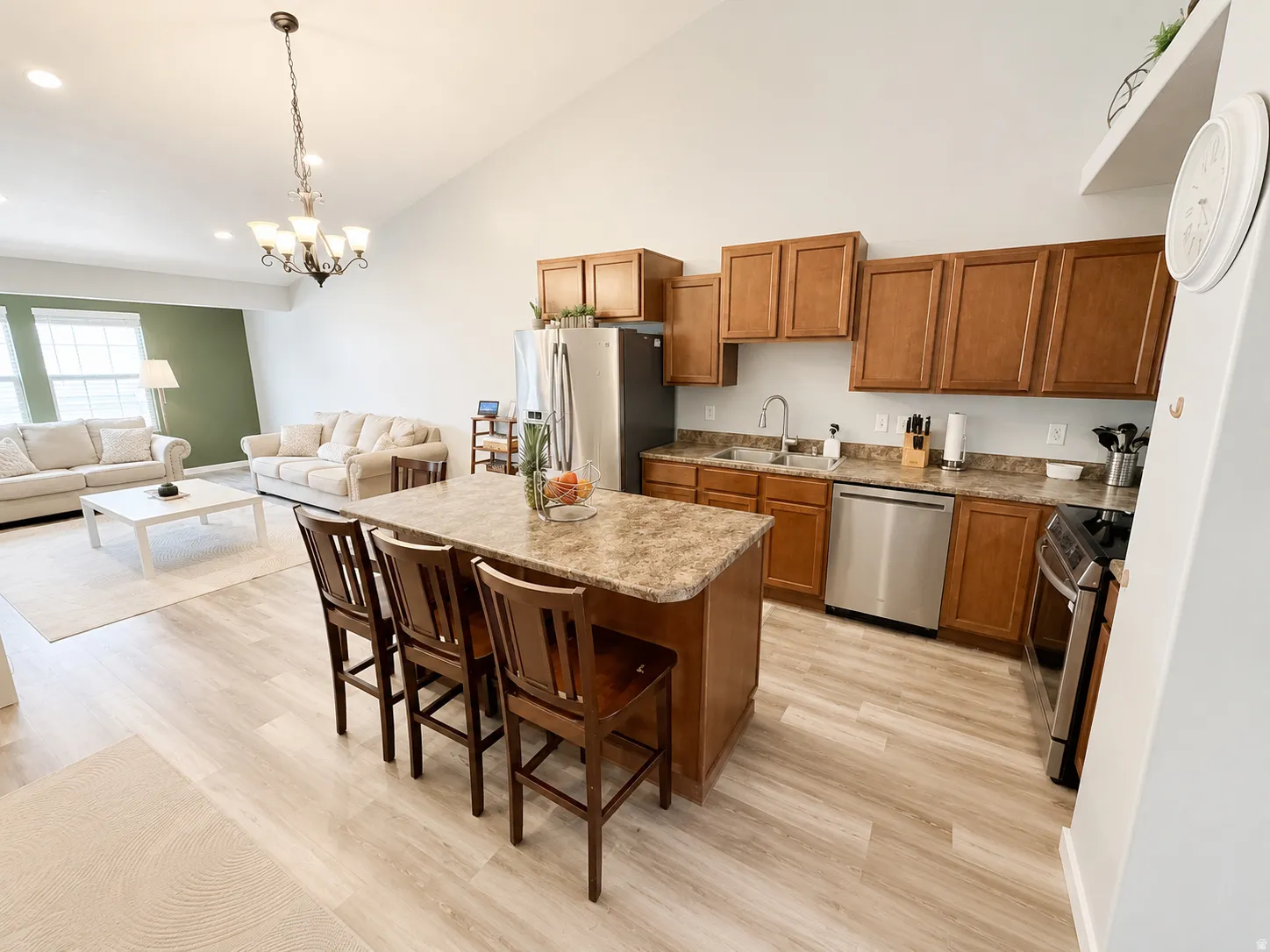 Open-concept kitchen and living area featuring vaulted ceilings, light wood-finish flooring, a kitchen island with seating, stainless steel appliances, and abundant natural light