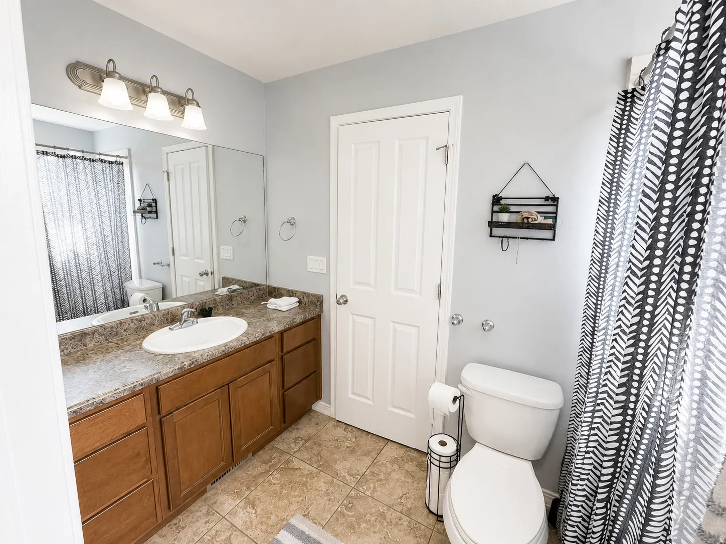 Bathroom featuring a spacious vanity with wood-finish cabinetry, a large mirror, and a three-light fixture