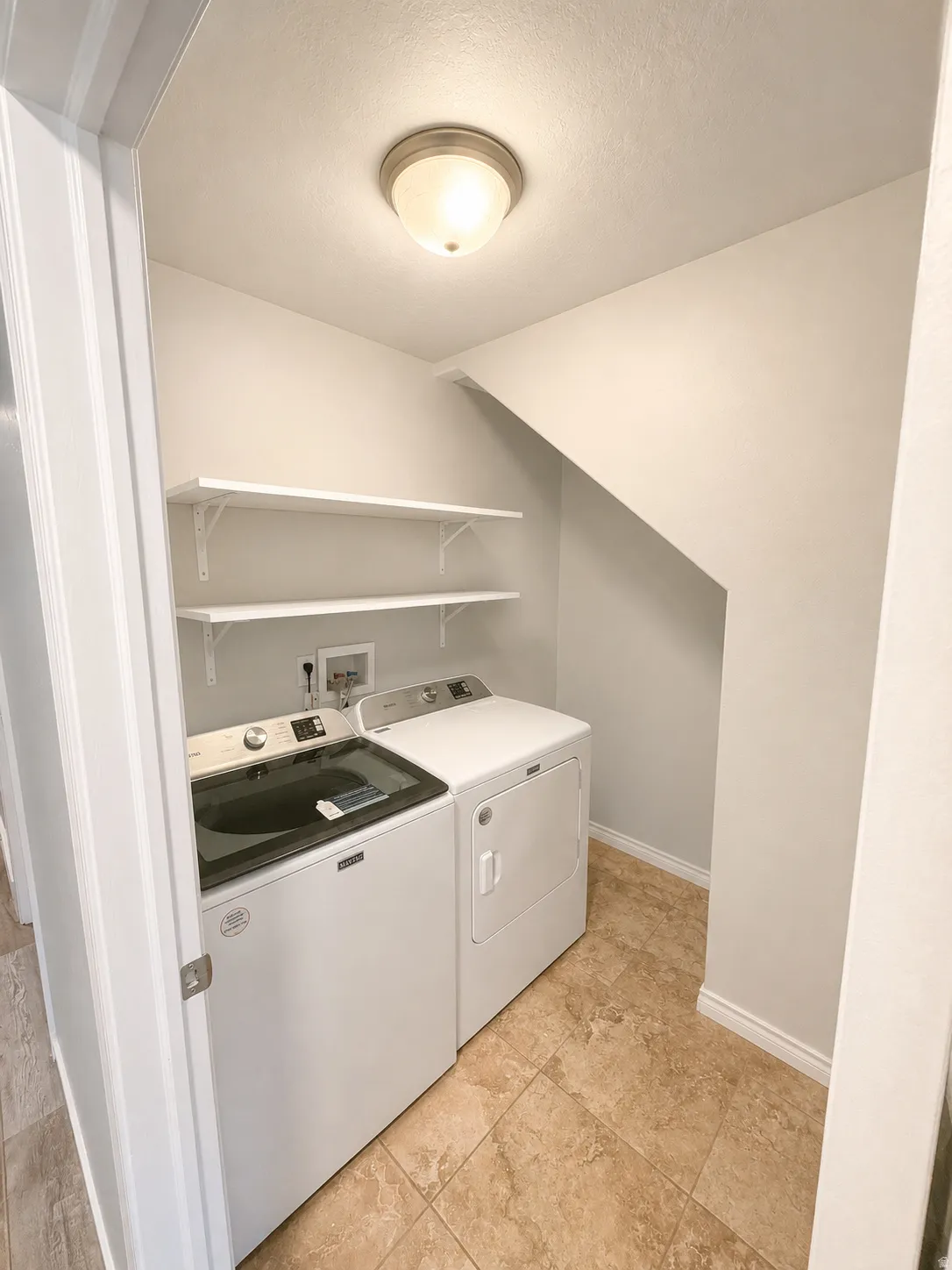 Dedicated laundry area featuring tiled flooring, a flush-mount ceiling light, and two white wall-mounted shelves