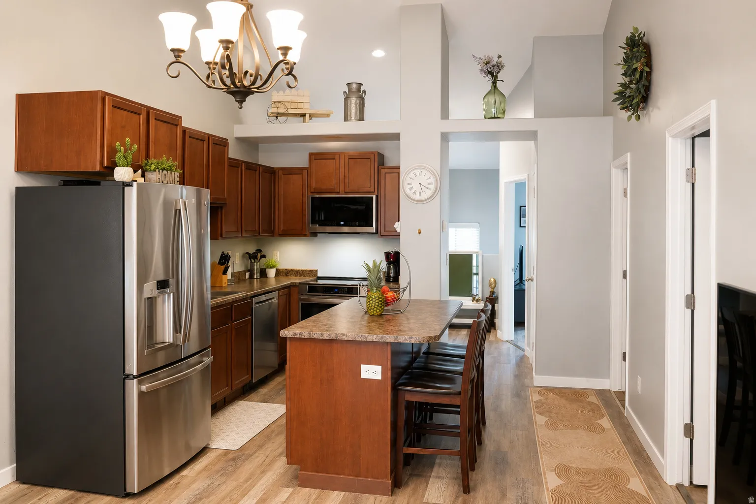 Kitchen featuring wood-finish flooring, stainless steel appliances, dark wood cabinetry, a breakfast bar island with seating, and vaulted ceilings