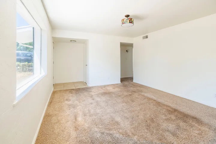 Spacious carpeted room featuring a large window, neutral wall tones, and recessed entry with tile flooring