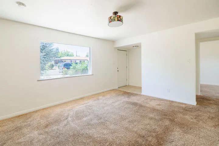 Carpeted living space featuring a picture window, neutral wall finishes, a ceiling-mounted light fixture, and an entry door with adjacent tile flooring