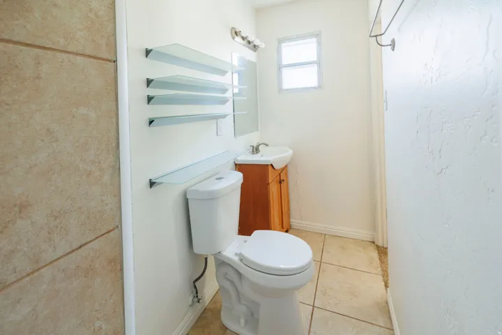Bathroom featuring a pedestal sink with a wood-finish vanity, tiled flooring, and multiple wall-mounted glass shelves