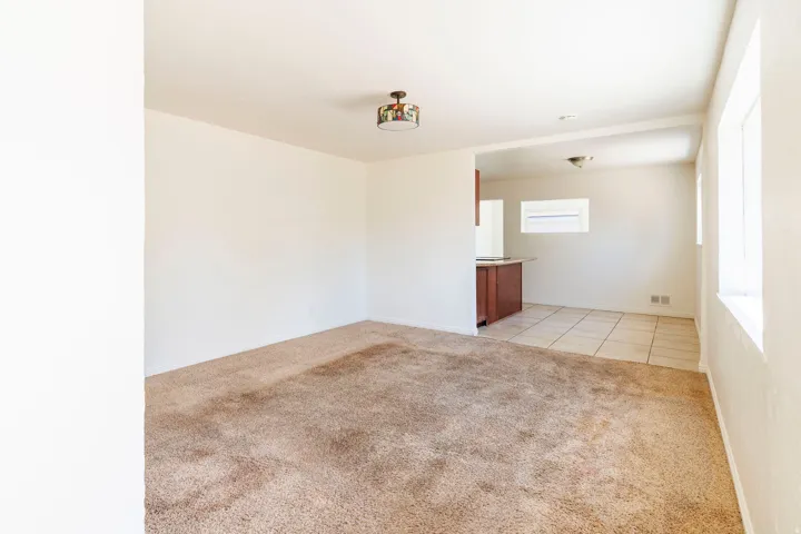 Bright living space featuring carpet flooring and a semi-open layout to a kitchen area with tile flooring and wood-finish cabinetry